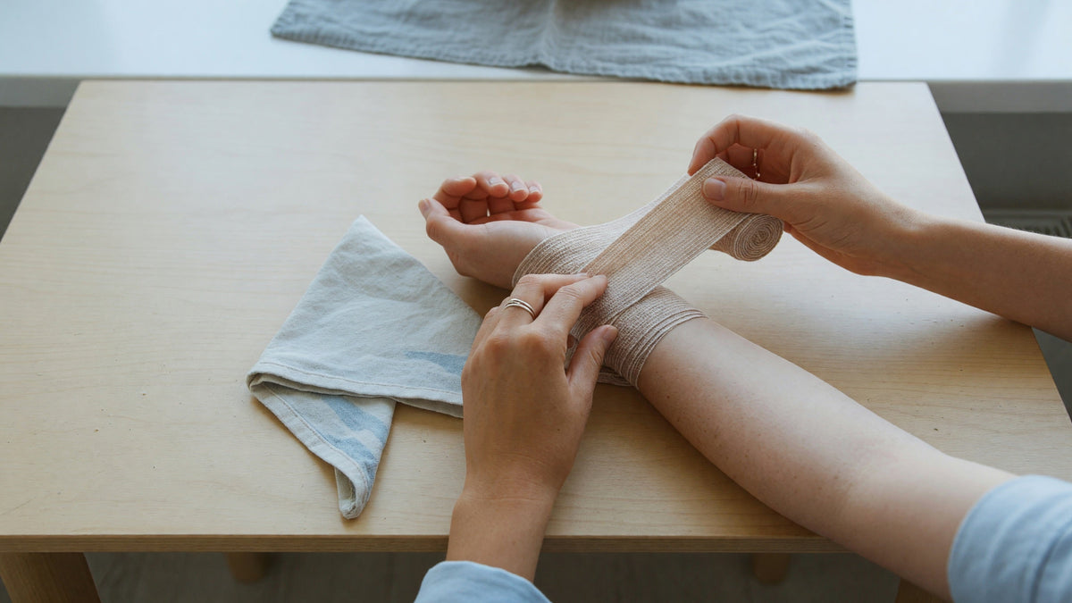 Händer lindar en elastisk binda runt en underarm