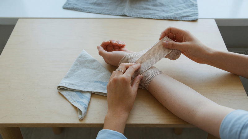Händer lindar en elastisk binda runt en underarm
