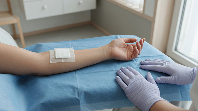 En underarm vilar på ett blått underlägg med ett tejpat förband på handryggen